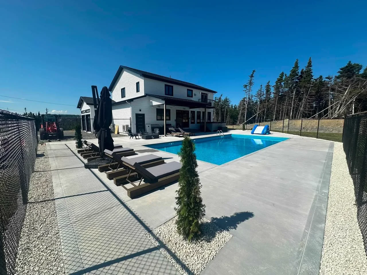 Finished blue in-ground pool with concrete deck and outdoor furniture